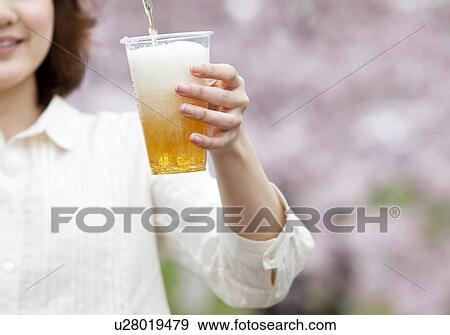 Stock Photo - Young woman pouring beer into plastic cup. Fotosearch
