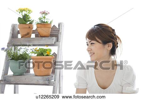 Stock Photo - Young woman sitting next to shelf with potted flowers. Fotosearch