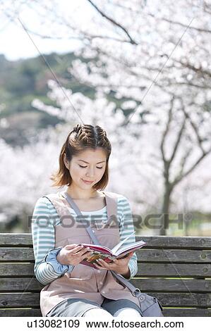 Stock Photo - Young woman sitting on bench reading a book. Fotosearch