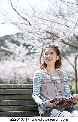 Stock Photo - Young woman sitting on bench reading a book. Fotosearch