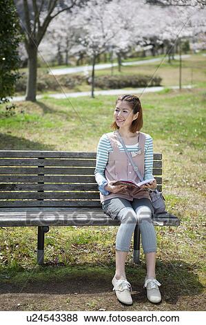 Young woman sitting on bench reading a book View Large Photo Image Stock Photo - Young woman sitting on bench reading a book. Fotosearch