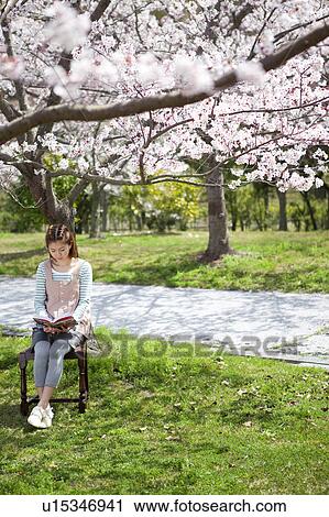 Stock Image - Young Woman sitting on chair reading a book. Fotosearch