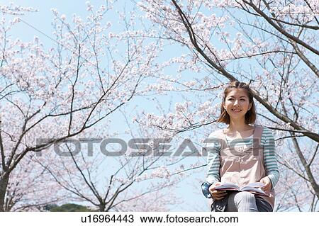 Stock Image - Young Woman sitting on chair reading a book. Fotosearch
