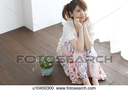 Stock Image - Young woman sitting on floor and head in hands. Fotosearch