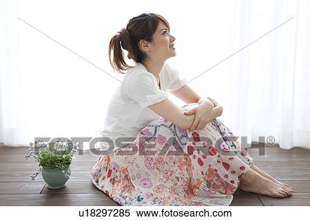 Stock Photography - Young woman sitting on floor and looking up. Fotosearch