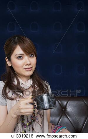 Stock Photograph - Young woman sitting on sofa holding a cup. Fotosearch