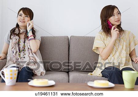 Young woman sitting on sofa on cell phone View Large Photo Image Stock Image - Young woman sitting on sofa on cell phone. Fotosearch