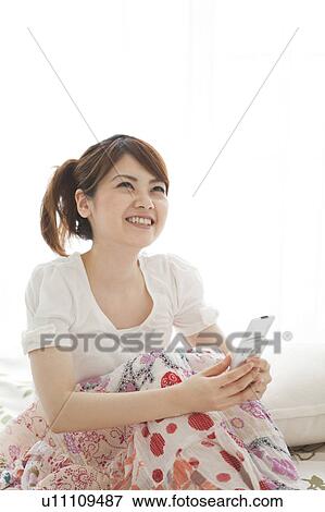 Young woman using cell phone on bed View Large Photo Image Stock Photo - Young woman using cell phone on bed. Fotosearch