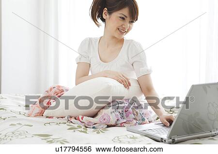 Stock Photograph - Young woman using laptop on bed. Fotosearch