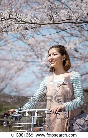 Stock Photography - Young woman with bicycle standing near cherry trees. Fotosearch