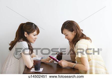 Stock Image - Young women at a cafe text messaging. Fotosearch