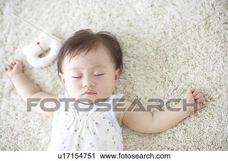 Stock Image - Baby lying down on carpet sleeping. Fotosearch
