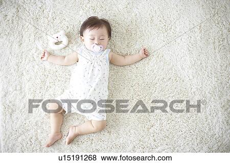 Stock Photo - Baby lying down on carpet sleeping. Fotosearch