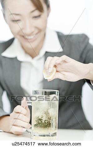 Stock Photo - Businesswoman squeezing lemon into highball, Tokyo Prefecture, Japan. Fotosearch
