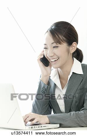 Stock Image - Businesswoman using a laptop and cell phone, Tokyo Prefecture, Japan. Fotosearch