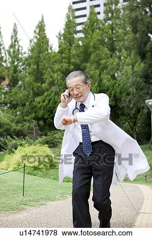 Doctor Running Whilst Talking On The Phone and Checking The Time View Large Photo Image Stock Photo - Doctor Running Whilst Talking On The Phone and Checking The Time. Fotosearch