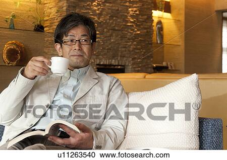 Stock Image - Mature Man Having Coffee Whilst Reading Book. Fotosearch