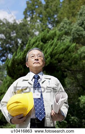 Stock Image - Mature Man Holding Hardhat And Blueprint. Fotosearch