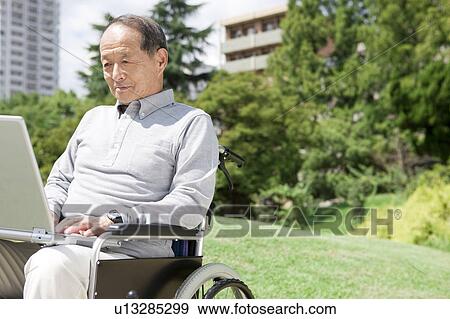 Stock Photo - Mature Man in Wheelchair Using Laptop. Fotosearch