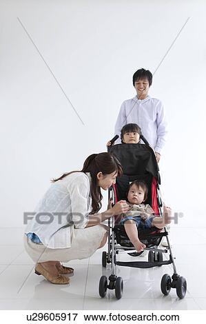 Stock Photo - Mother Beside Baby Boy in Buggy, Father and Daughter in the Background. Fotosearch