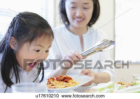 Stock Image - Mother Giving Pasta to Hungry Daughter. Fotosearch