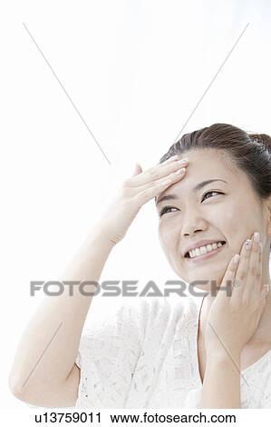 Stock Image - Young woman applying moisturizer on face, Tokyo Prefecture, Honshu, Japan. Fotosearch