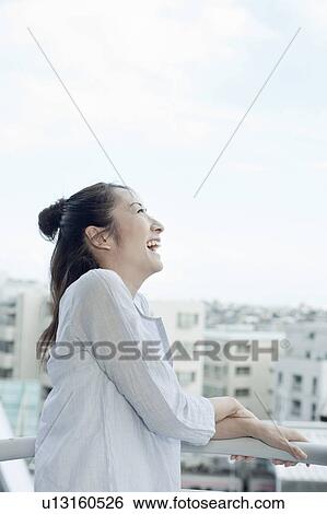 Stock Photograph - Young woman at balcony laughing, Tokyo Prefecture, Japan. Fotosearch