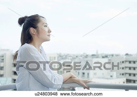 Stock Photo - Young woman at balcony looking at cityscape, Tokyo Prefecture, Japan. Fotosearch