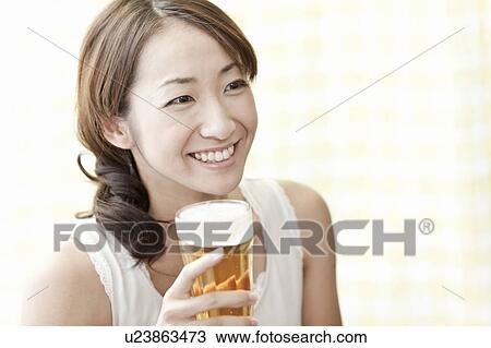 Stock Image - Young woman holding a glass of beer, Tokyo Prefecture, Japan. Fotosearch