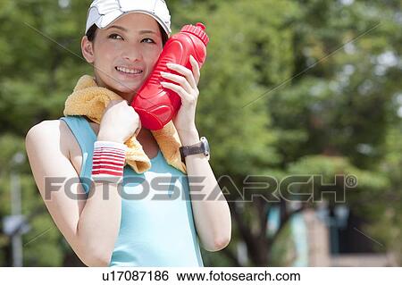 Stock Photograph - Young Woman Holding Water Bottle Against Her Cheek. Fotosearch