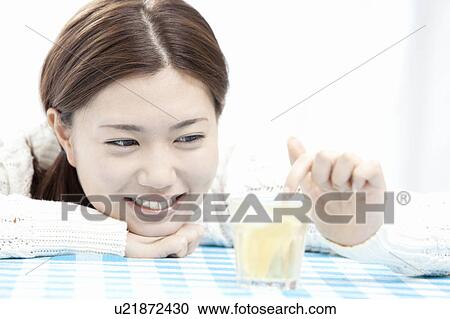 Stock Image - Young woman mixing drink with finger, Tokyo Prefecture, Honshu, Japan. Fotosearch