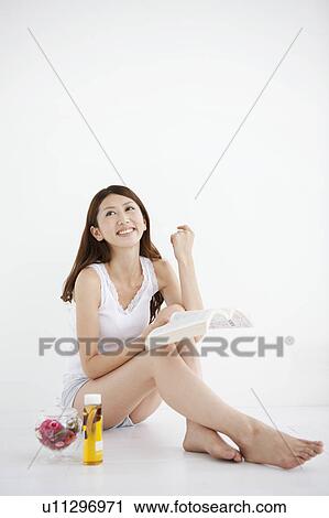 Stock Image - Young Woman Sitting By Toiletries and Reading Book. Fotosearch