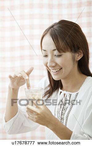 Stock Photo - Young woman touching ice cube in glass of water, Tokyo Prefecture, Japan. Fotosearch