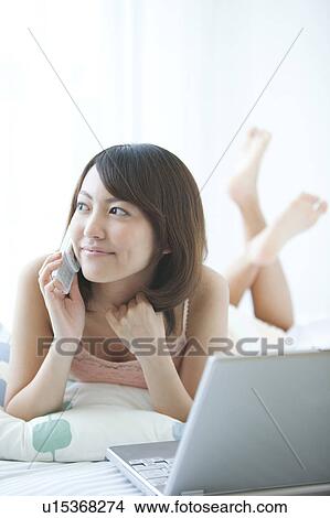Picture - Young Woman Using Laptop and Mobile Phone in Bed. Fotosearch