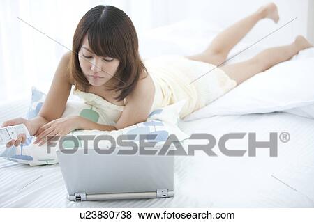 Stock Photo - Young Woman Using Laptop and Mobile Phone in Bed. Fotosearch