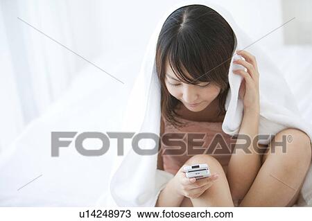 Stock Image - Young Woman Using Mobile Phone in Bed. Fotosearch