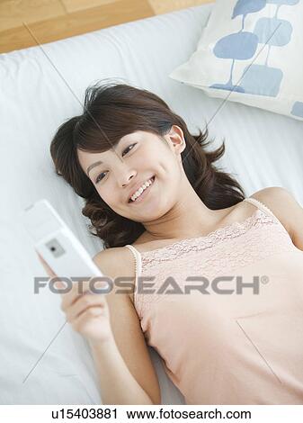 Stock Image - Young Woman Using Mobile Phone in Bed. Fotosearch