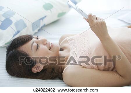 Stock Image - Young Woman Using Mobile Phone in Bed. Fotosearch