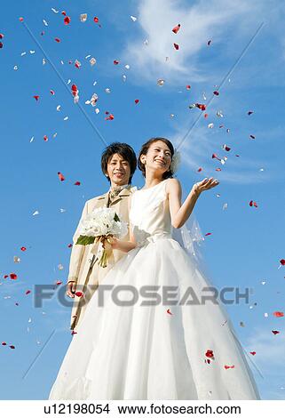 Picture - Bride and bridegroom looking at flower petals in the air. Fotosearch