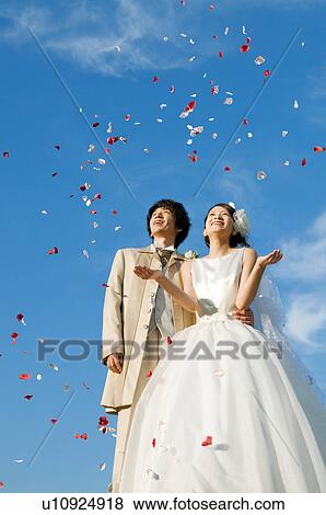 Stock Photo - Bride and bridegroom looking at flower petals in the air. Fotosearch