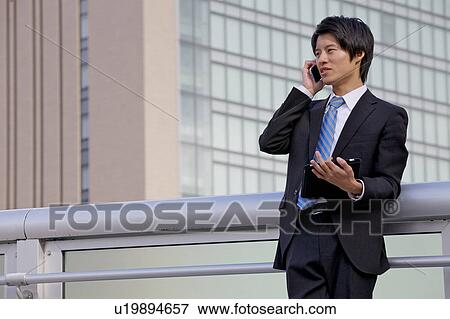Stock Photo - Businessman on mobile phone and using digital tablet outdoors. Fotosearch