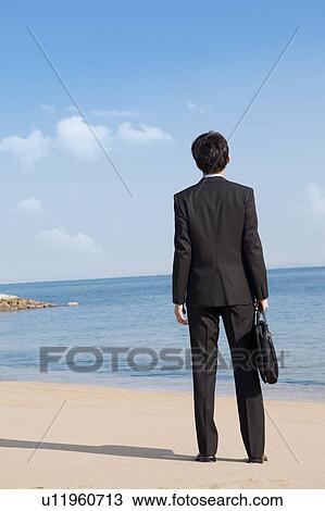 Businessman standing on the beach, rear view View Large Photo Image Stock Image - Businessman standing on the beach, rear view. Fotosearch