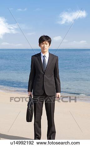 Stock Image - Businessman standing on the beach. Fotosearch
