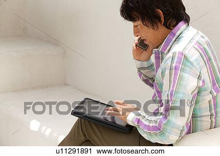 Stock Image - Mature man on a mobile phone using a digital tablet . Fotosearch