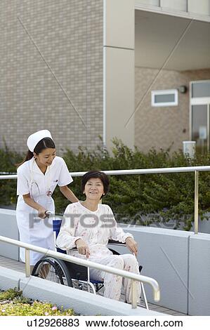 Stock Image - Nurse Pushing Patient in Wheelchair. Fotosearch