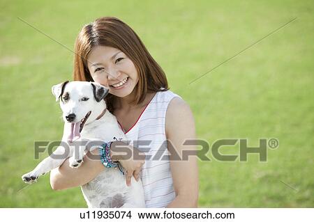 Picture - Portrait of young woman carrying a dog. Fotosearch