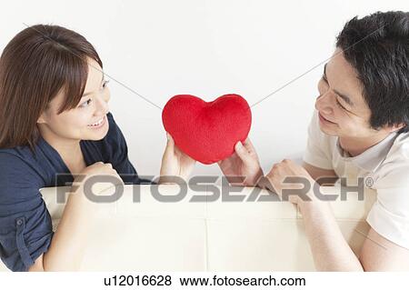 Young couple sitting on sofa holding a heart View Large Photo Image Stock Photo - Young couple sitting on sofa holding a heart. Fotosearch