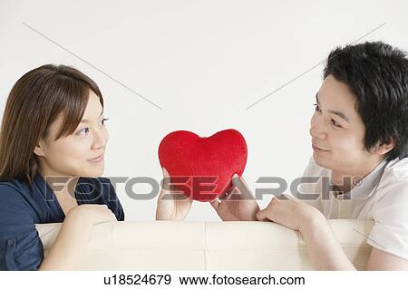 Young couple sitting on sofa holding a heart View Large Photo Image Stock Photo - Young couple sitting on sofa holding a heart. Fotosearch