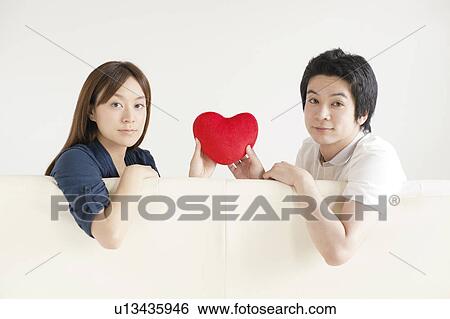 Young couple sitting on sofa holding a heart View Large Photo Image Stock Photograph - Young couple sitting on sofa holding a heart. Fotosearch