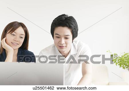Stock Image - Young couple sitting on sofa using laptop. Fotosearch